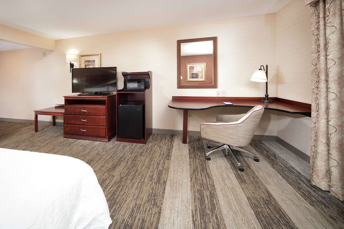 A hotel room with a bed, a desk with a computer, a TV, a microwave, and a lamp.