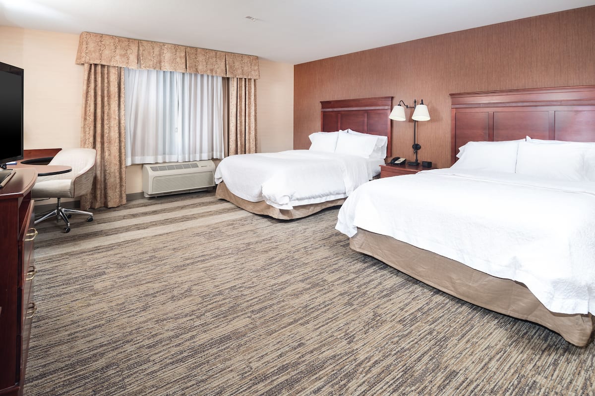 A hotel room with two beds, a desk, a chair, a TV, and a window with curtains.
