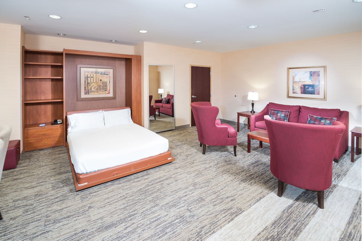 A hotel room with a bed, a red armchair, a sofa, a small table, and a mirror.