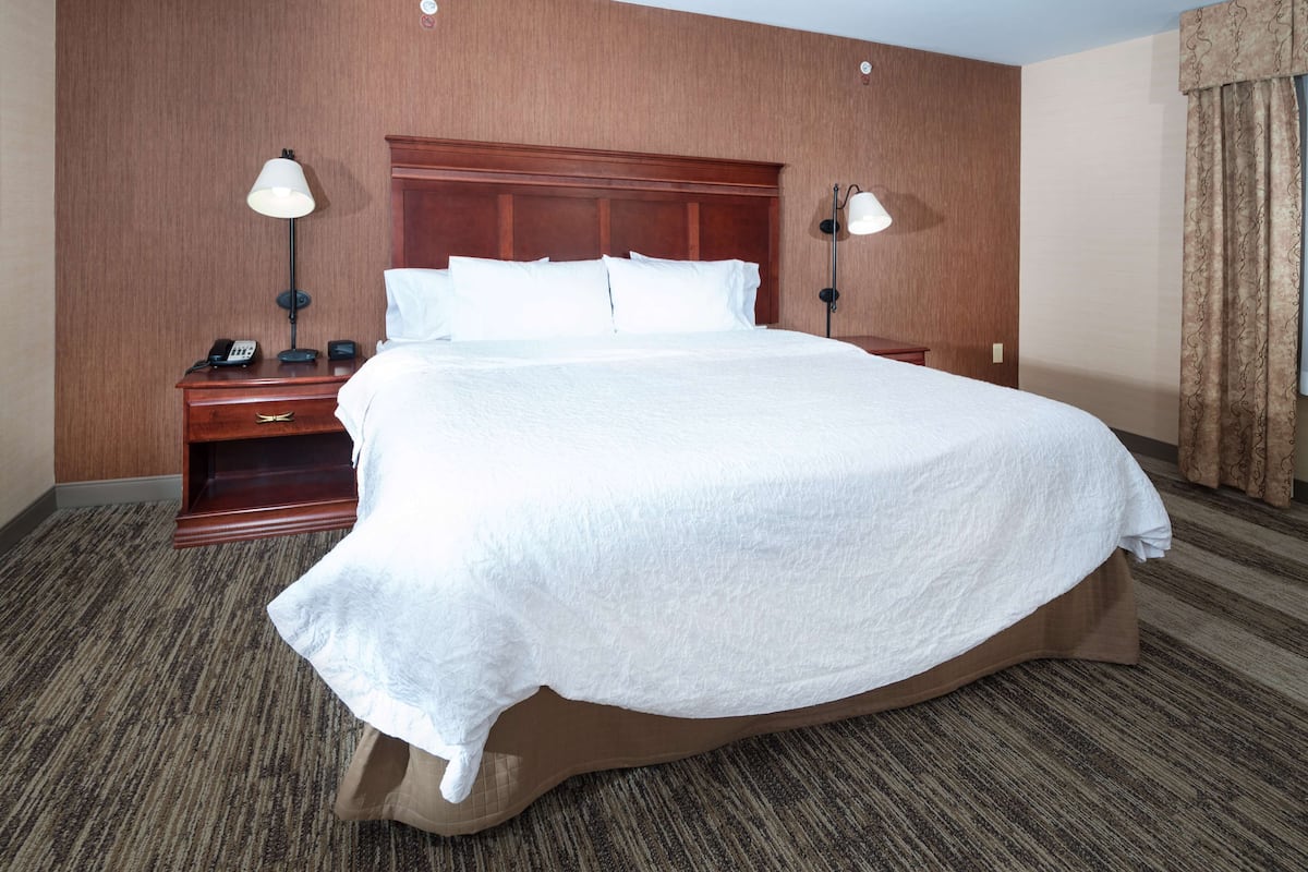A hotel room with a large bed, wooden headboard, two bedside tables with lamps, and a carpeted floor.