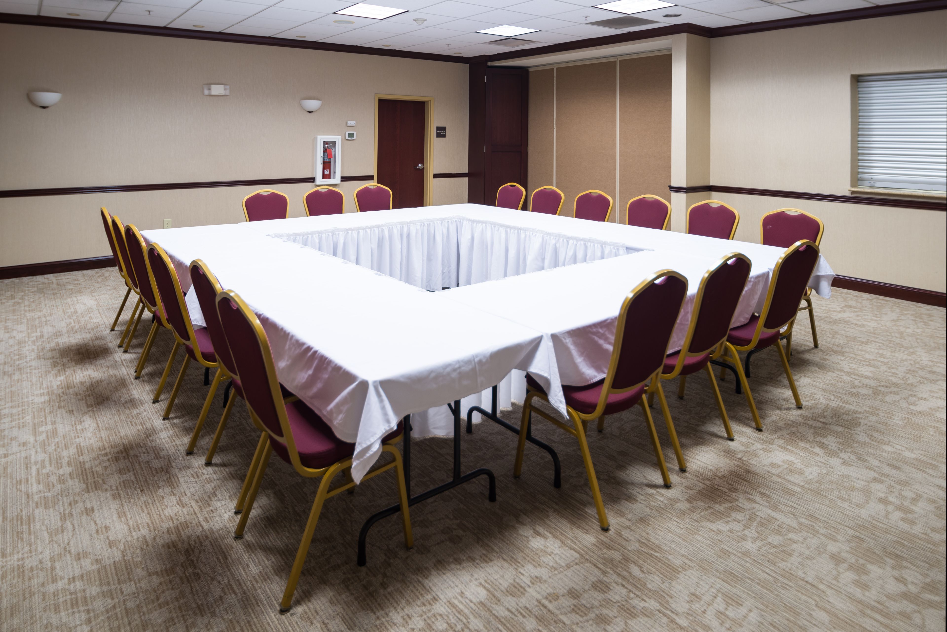 A conference room with a large rectangular table surrounded by chairs, carpeted floor, and a door in the background.
