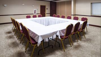 A conference room with a large rectangular table surrounded by chairs, carpeted floor, and a door in the background.