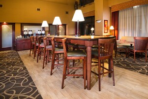 Uma sala de jantar de hotel com uma longa mesa de madeira, várias cadeiras e luminárias.
