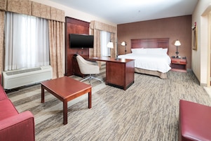 Quarto de hotel com cama, escrivaninha, cadeira, televisão e sofá vermelho.