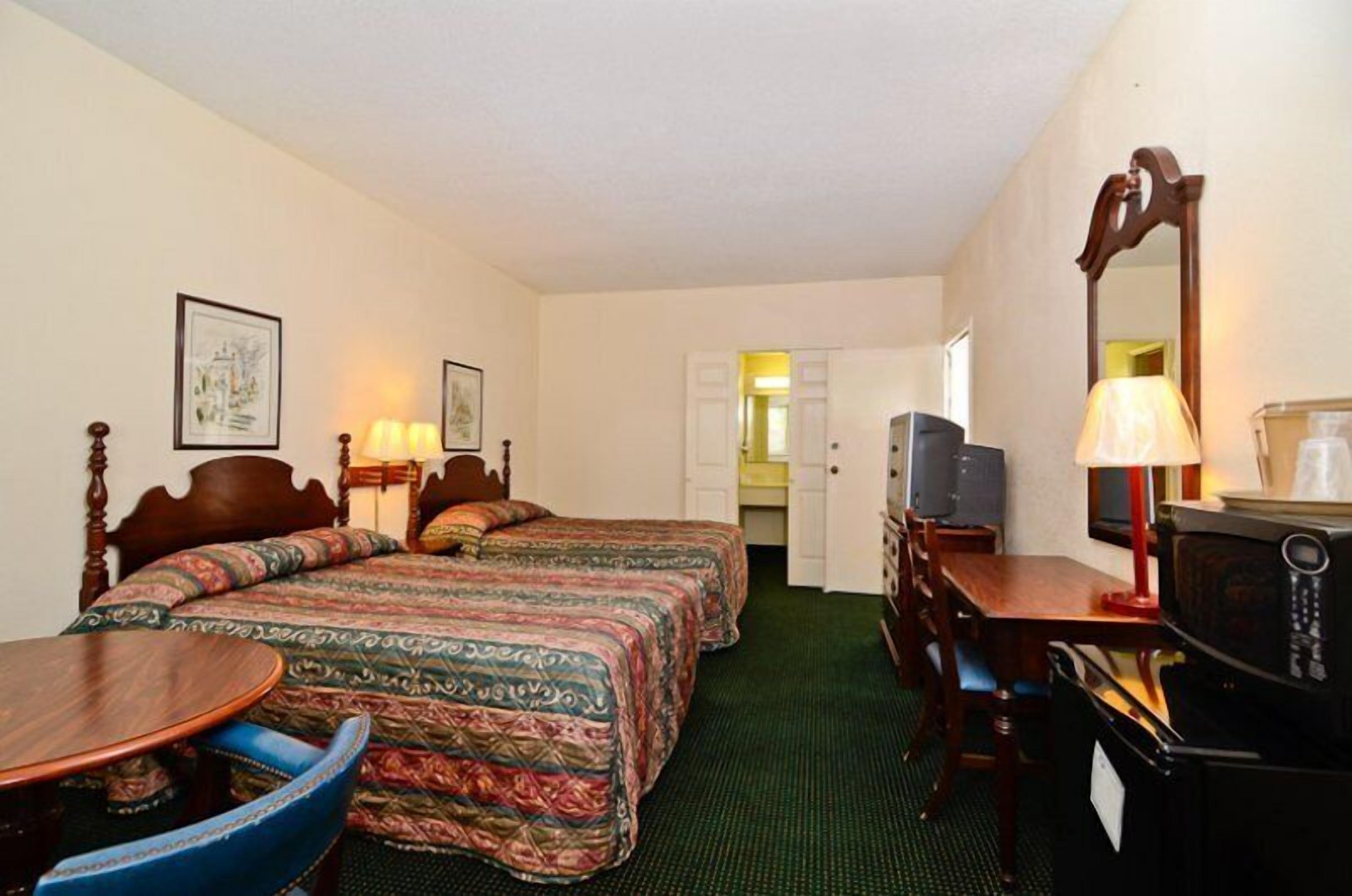 A hotel room with two beds, a desk, a chair, a television, and a microwave.