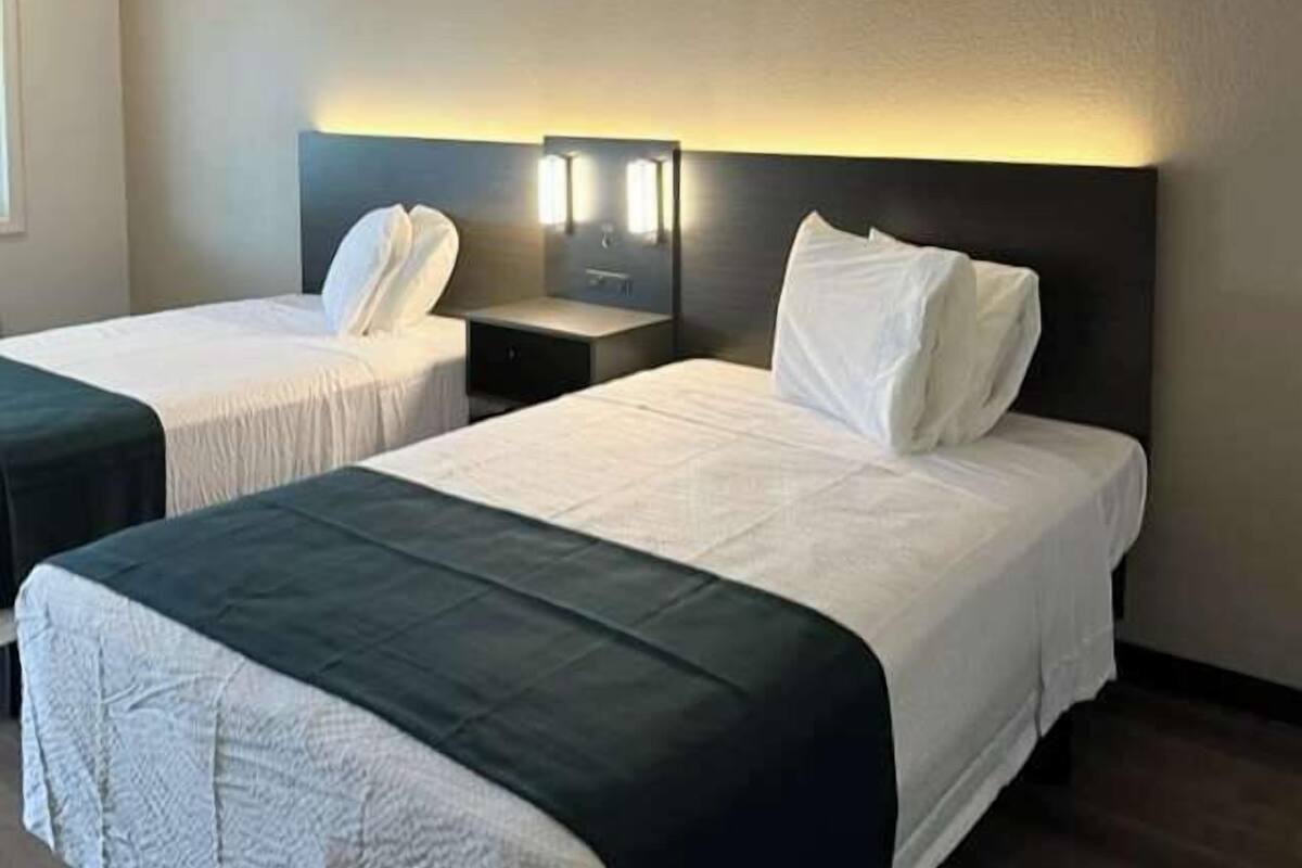 A hotel room with two beds, each with a pillow and a nightstand.