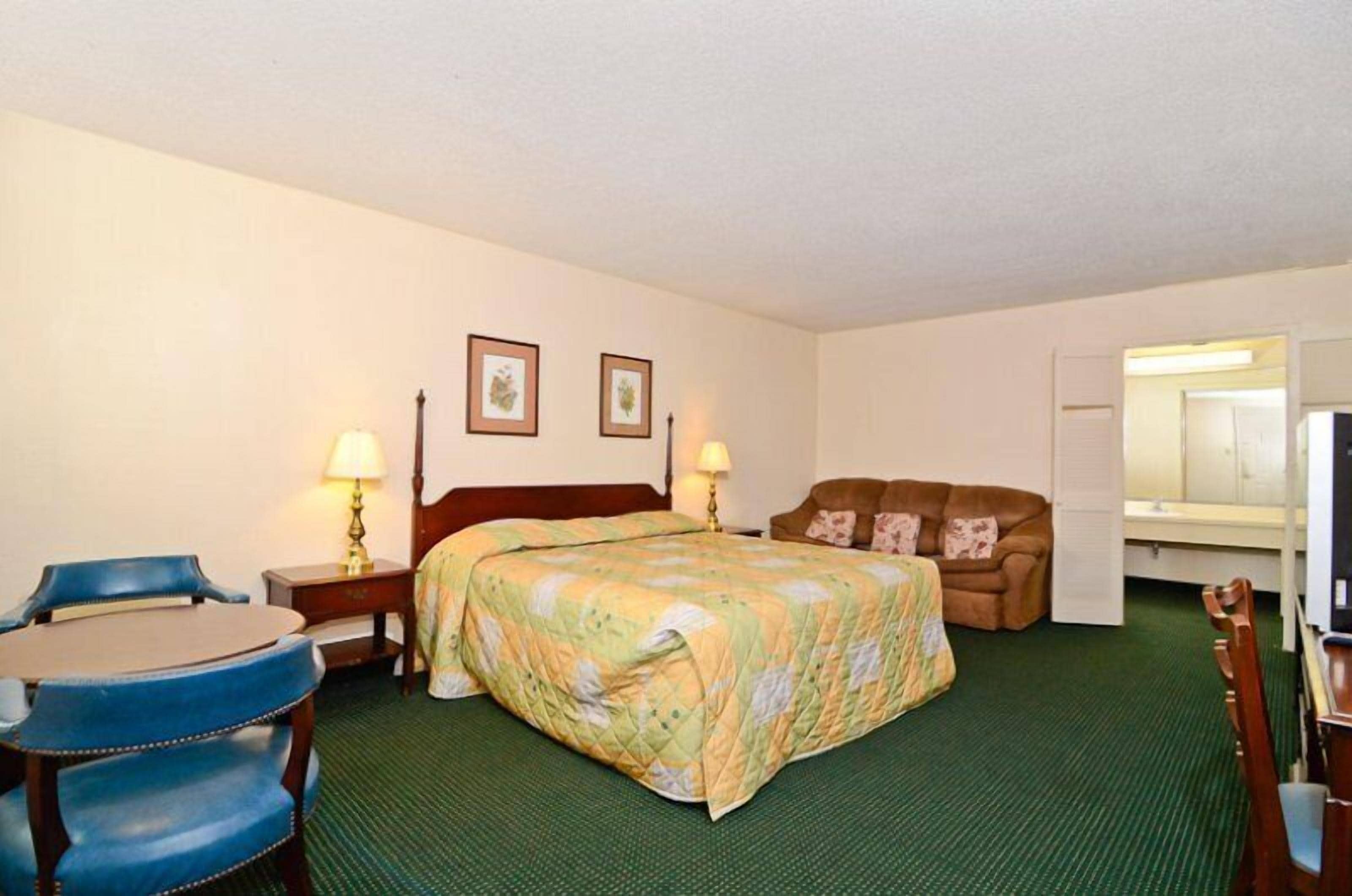 A hotel room with a bed, a desk with a chair, a couch, a lamp, and a mirror.