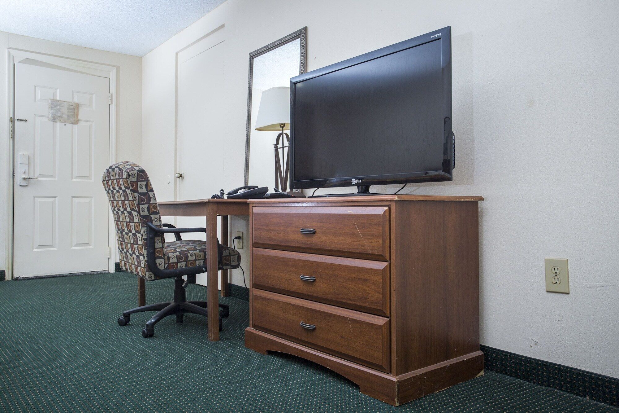 Hotellihuone, jossa on puinen työpöytä, tuoli, televisio ja peili.