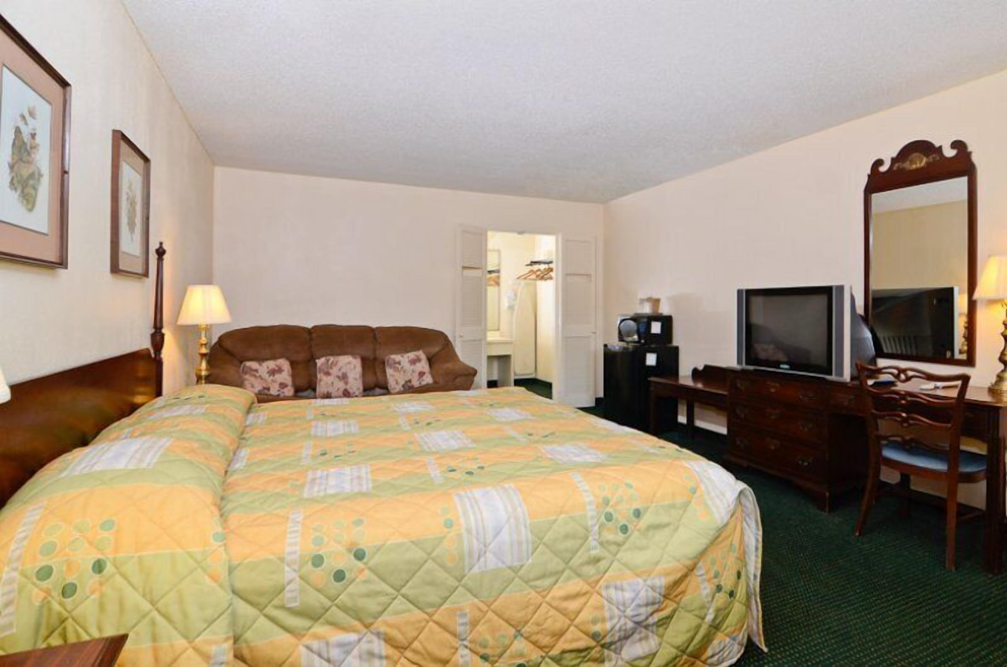 A hotel room with a large bed, a desk with a television, and a mirror.