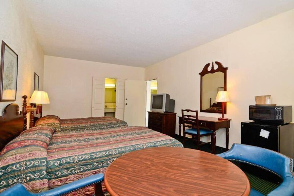 A hotel room with a large bed, a desk with a chair, a round table, a television, and a mirror.