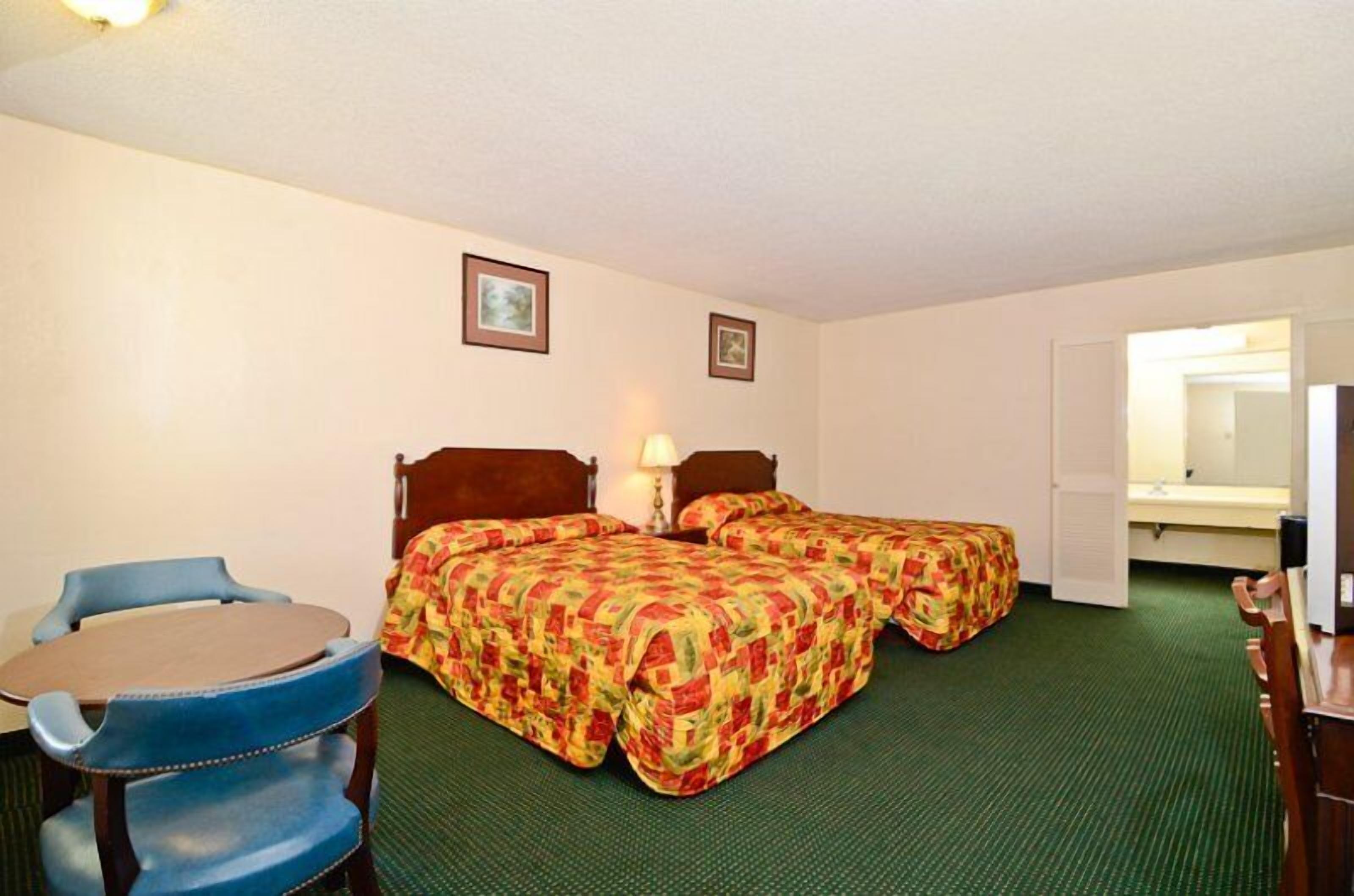 A hotel room with two single beds, a small table with chairs, a desk, and a mirror.