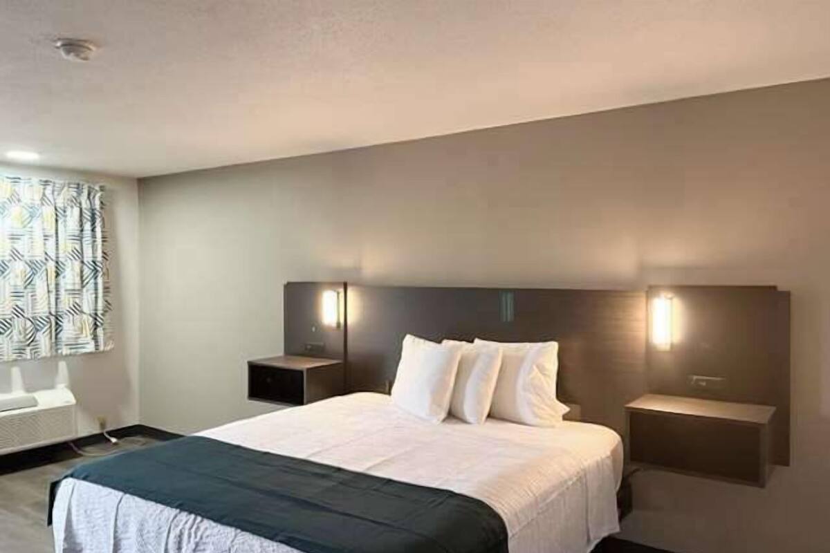 A hotel room with a large bed, two bedside tables, and a headboard with integrated lighting.