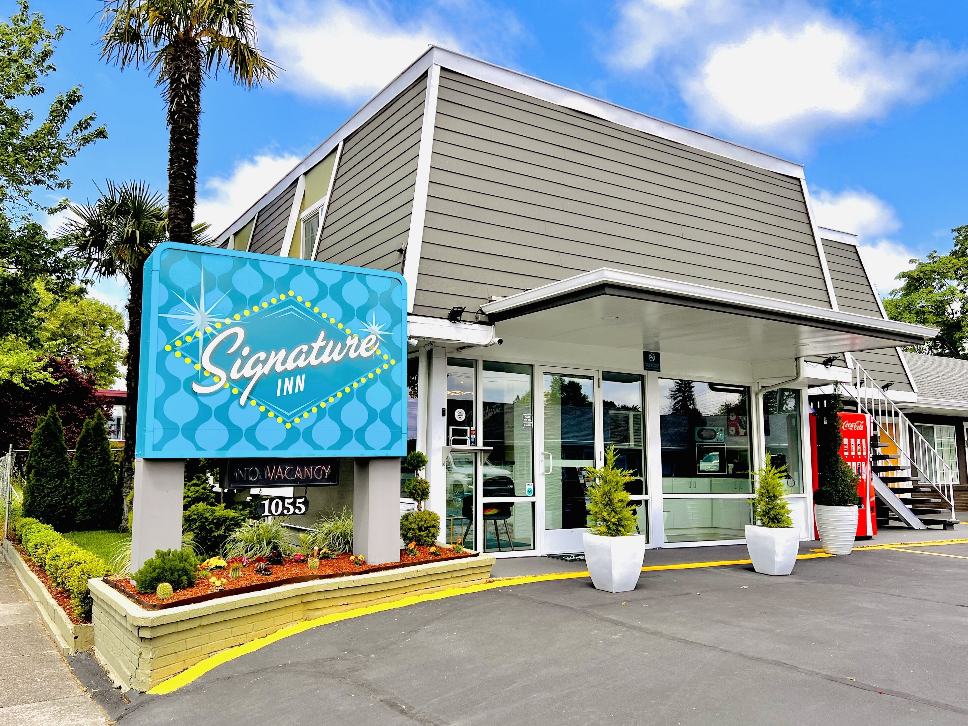 A Signature Inn building with a blue sign, glass entrance, and a Coca-Cola vending machine.