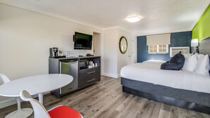A modern hotel room with a bed, a desk, a chair, a TV, and a kitchenette. - Signature Inn Eugene (Eugene)
