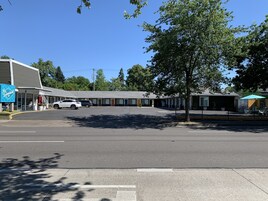 Un motel con una hilera de habitaciones, un estacionamiento y un pequeño espacio exterior con una tienda de campaña.