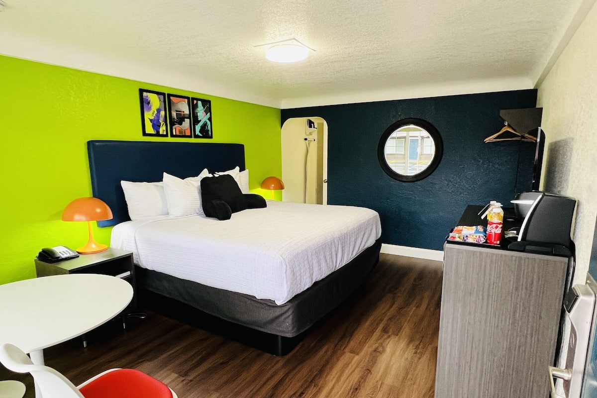 A hotel room with a bed, a desk, a chair, a wardrobe, and a round mirror.