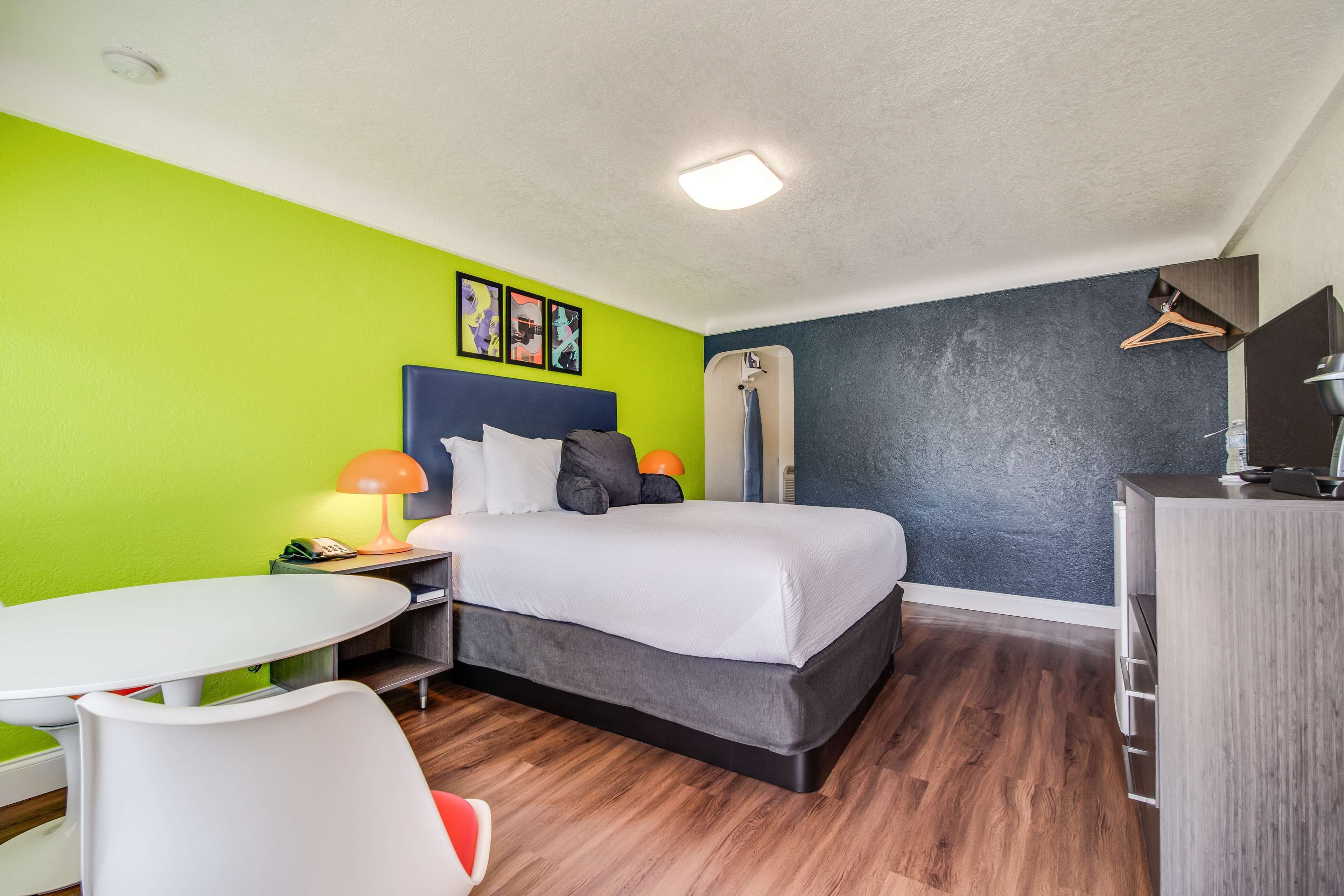 A modern hotel room with a bed, a desk, a chair, and a small table.
