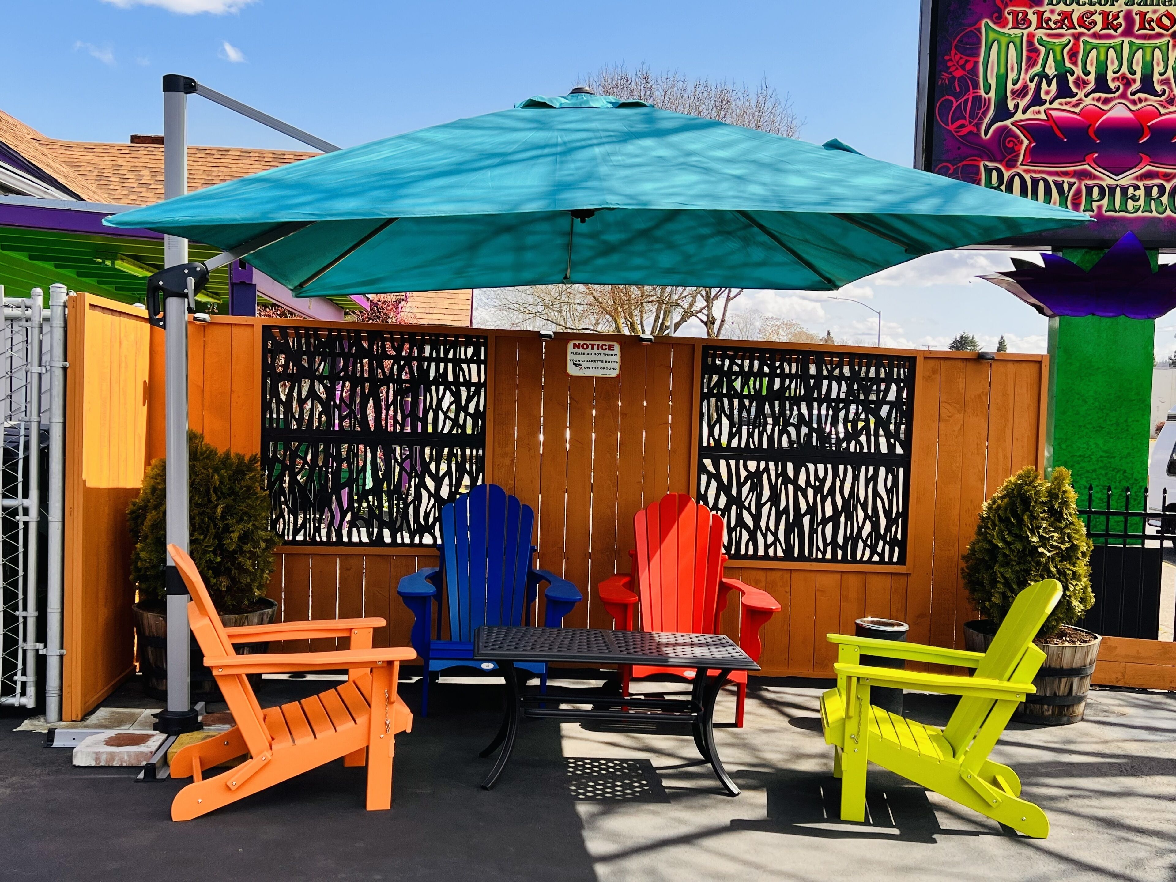 An outdoor seating area with colorful Adirondack chairs, a table, and a green umbrella.
