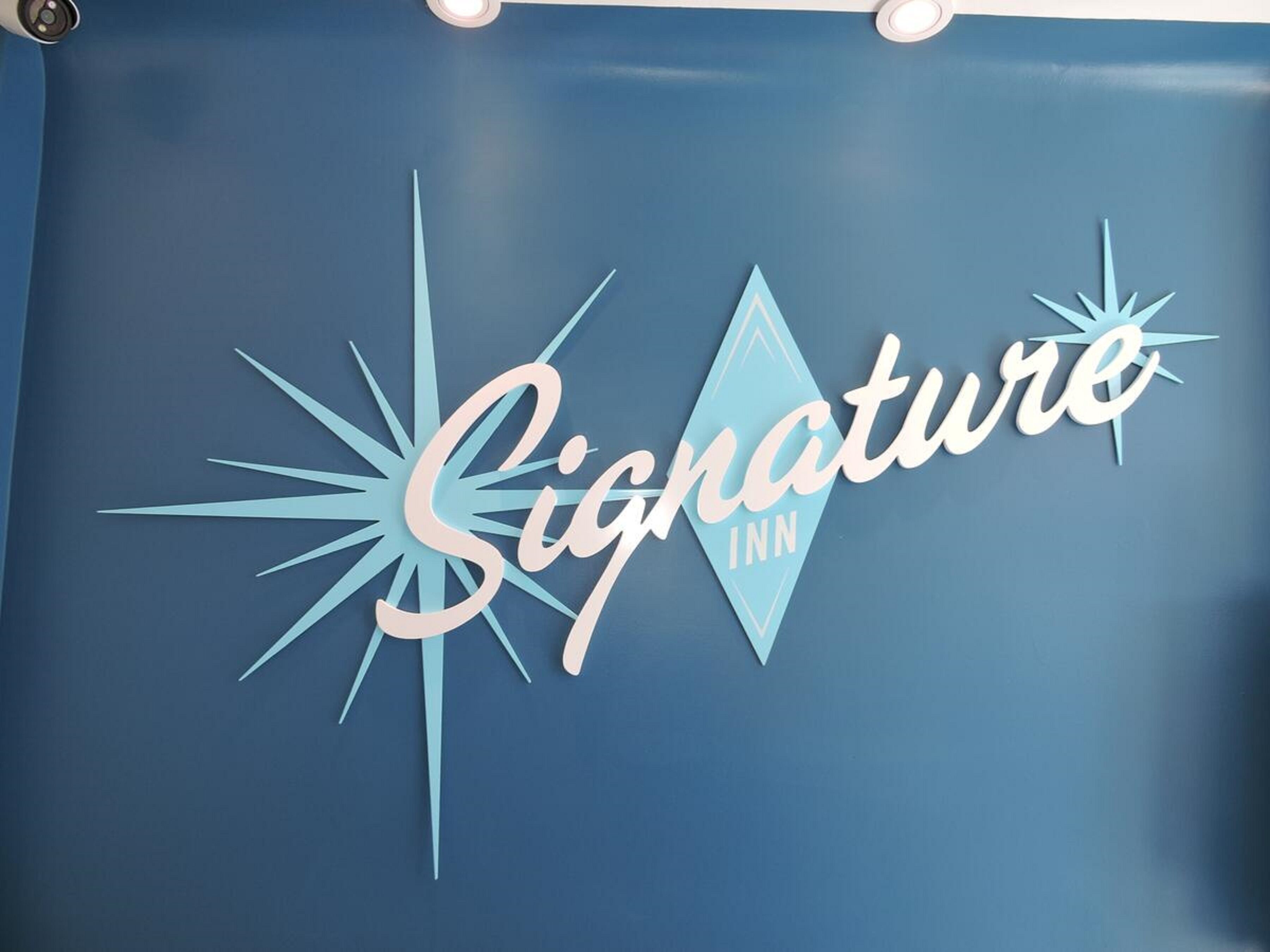 Eine blaue Wand mit dem Logo des Signature Inn, das ein strahlenförmiges Design und das Wort 'Signature' in Schreibschrift zeigt.