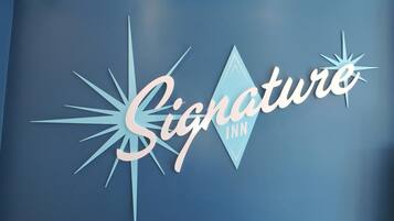 Eine blaue Wand mit dem Logo des Signature Inn, das ein strahlenförmiges Design und das Wort 'Signature' in Schreibschrift zeigt.