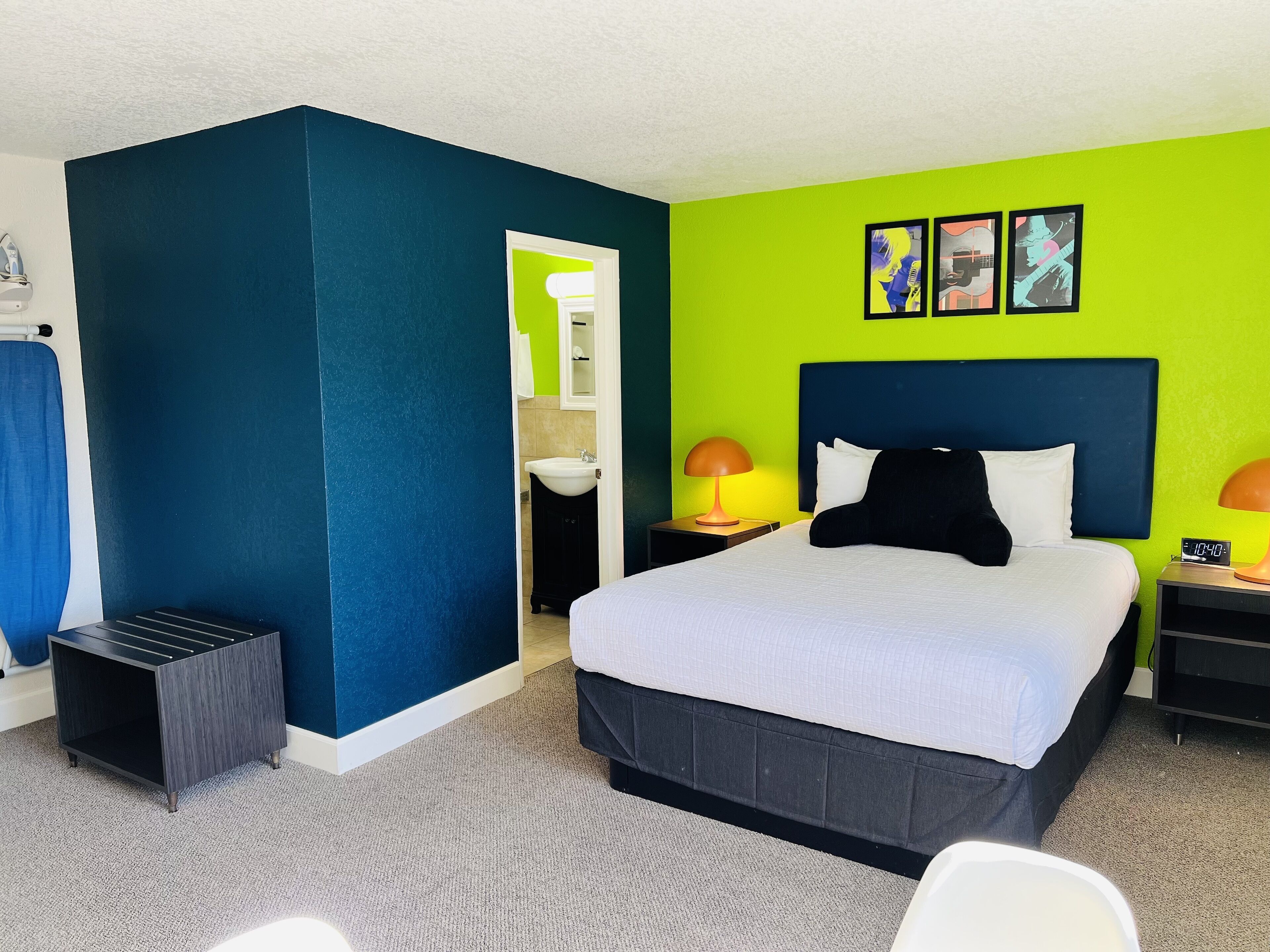 Habitación de hotel con cama, mesitas de noche, lámpara, reloj y obras de arte en la pared.