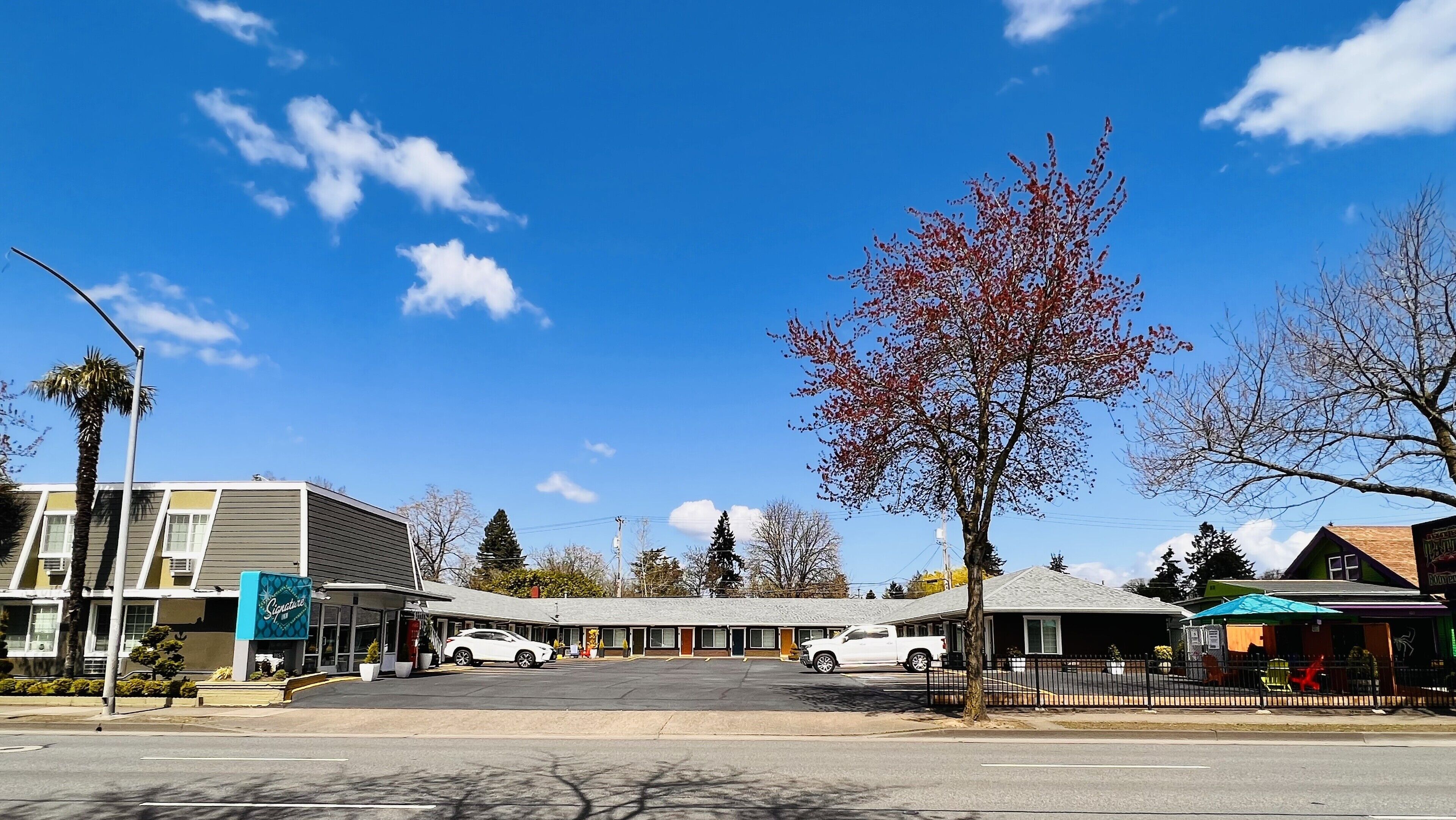 Un motel con un’area parcheggio centrale, una zona salotto coperta all'aperto e una fila di edifici a un piano dal design semplice.