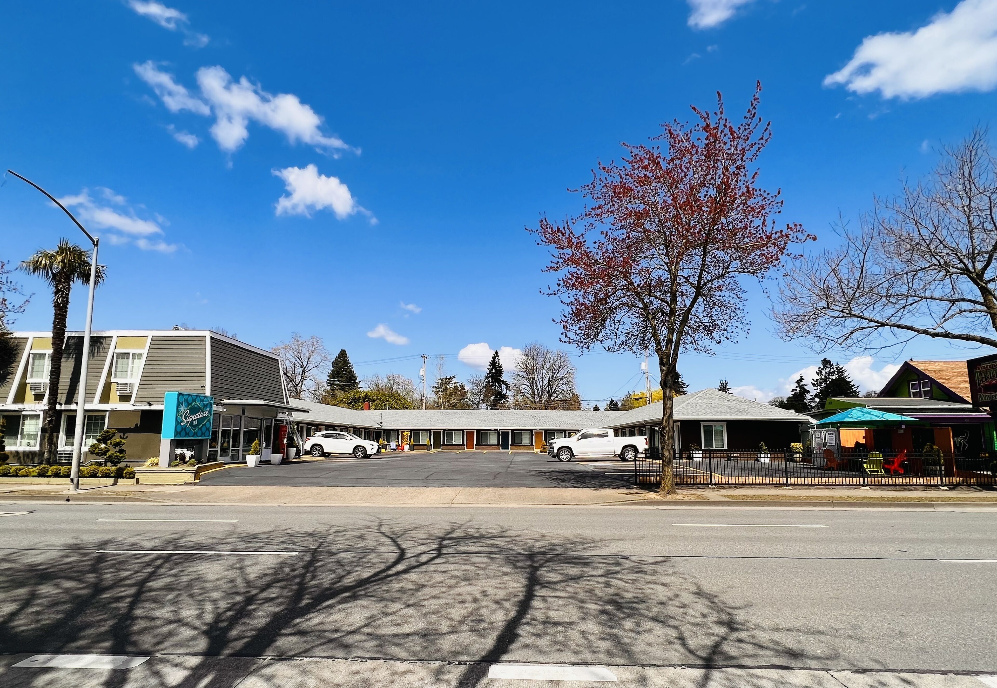 A motel with a central parking area, a small storefront, and a tree with red leaves.