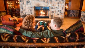 A cozy living room with a stone fireplace, comfortable seating, and a bar area in the background. - High Peaks Resort (Lake Placid)