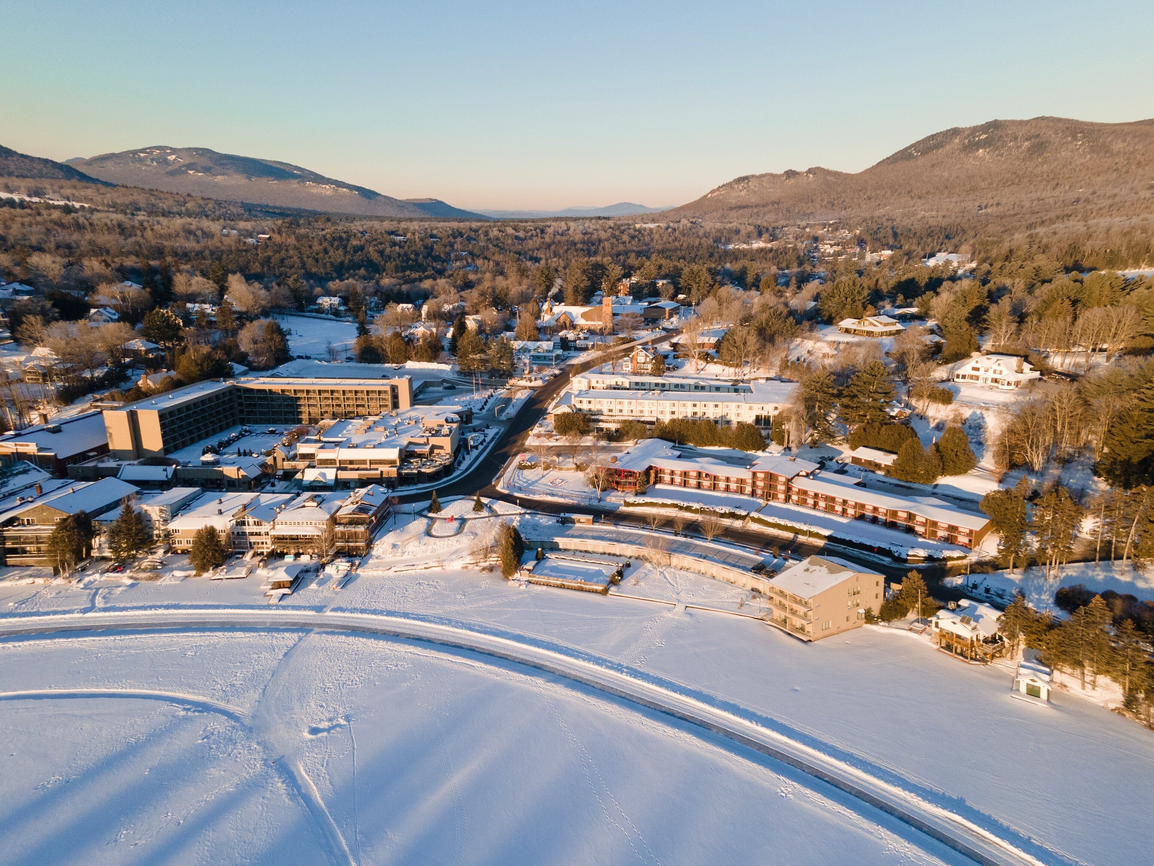 An aerial view of a town with snow-covered streets and buildings, surrounded by mountains.