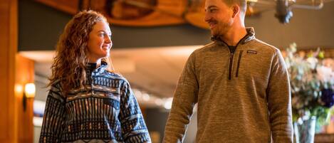 A couple holding hands in a warmly lit indoor setting with a wooden ceiling and a chandelier.