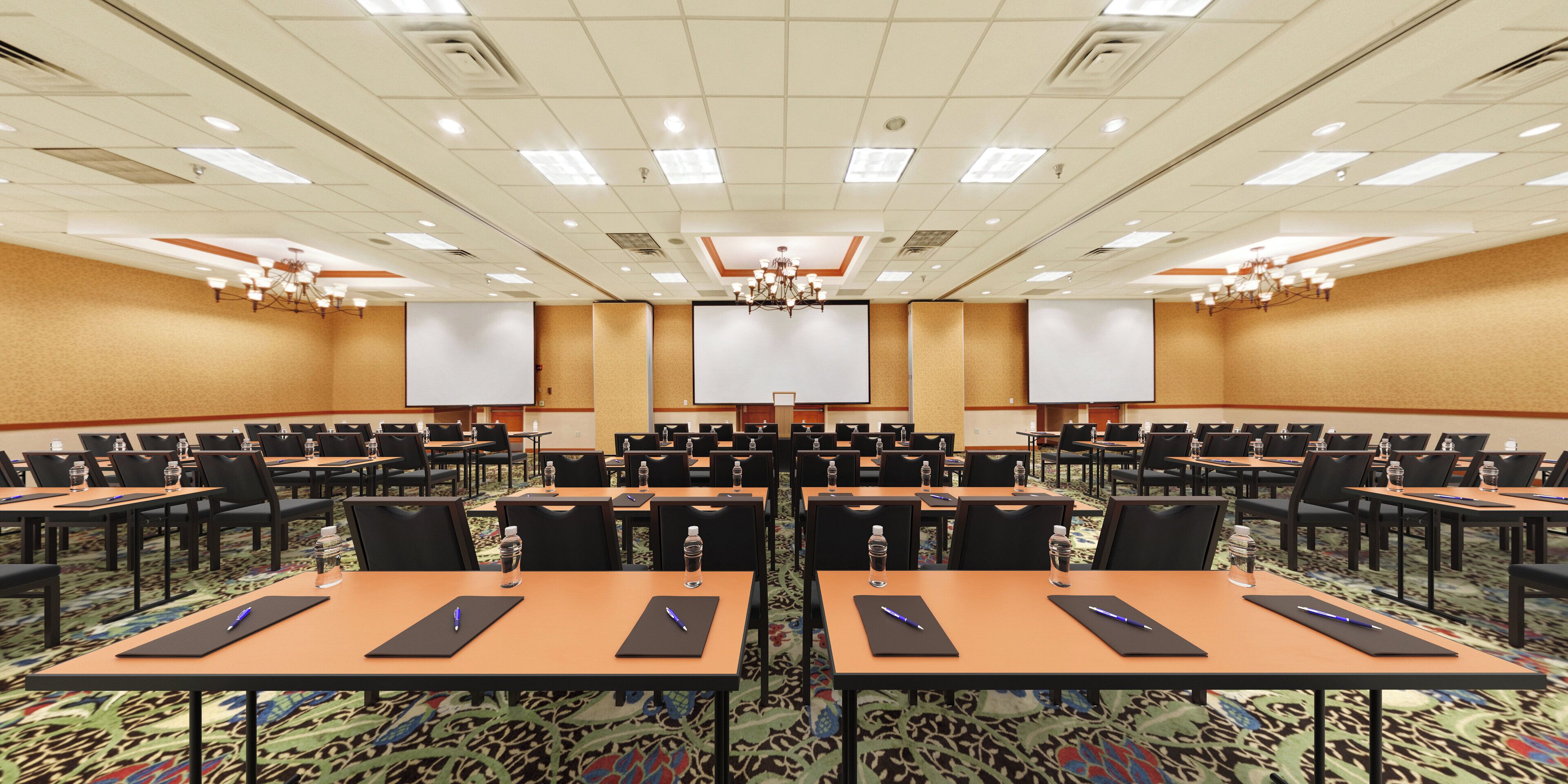 A conference room with rows of tables, chairs, and a large screen at the front.