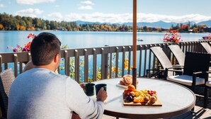 A man sitting at a round table with a view of a lake and mountains. - High Peaks Resort (Lake Placid)