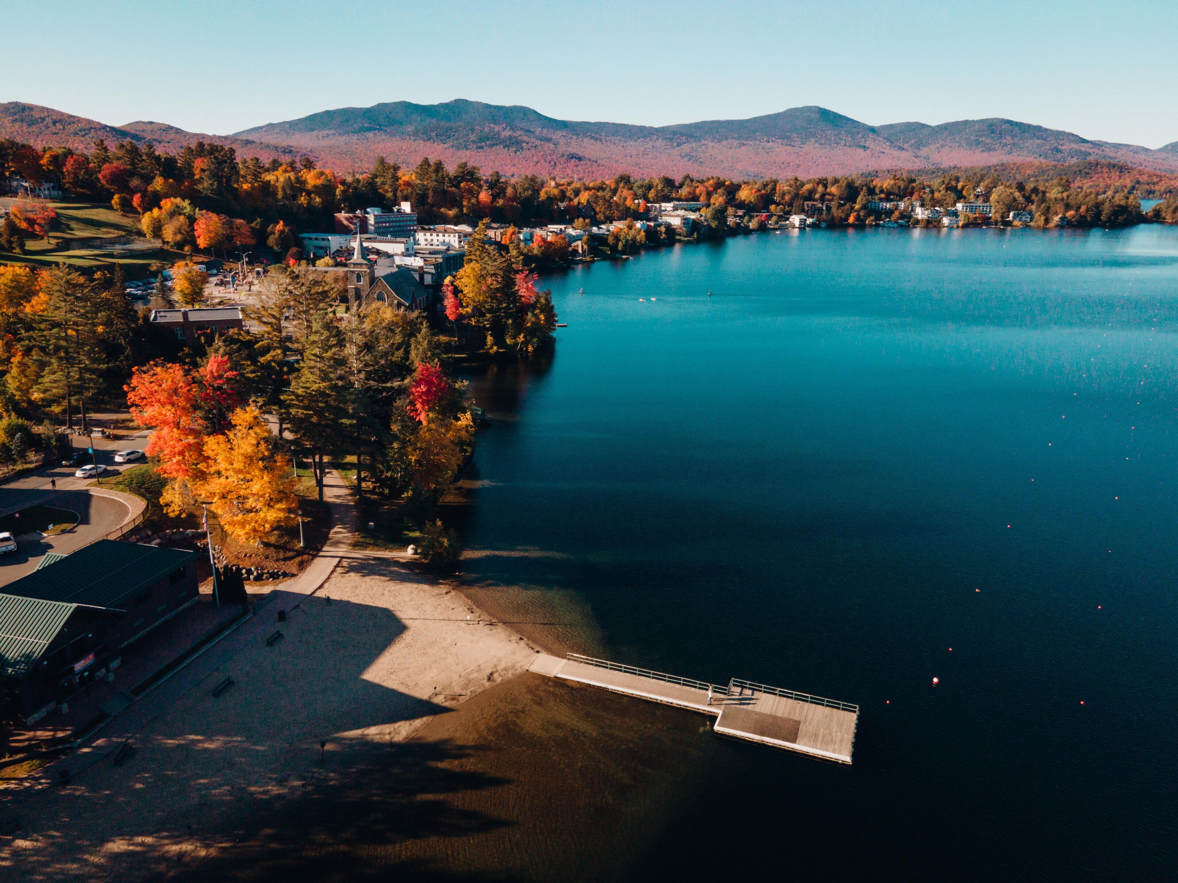 An aerial view of a lakeside town with a dock, buildings, and autumn foliage.