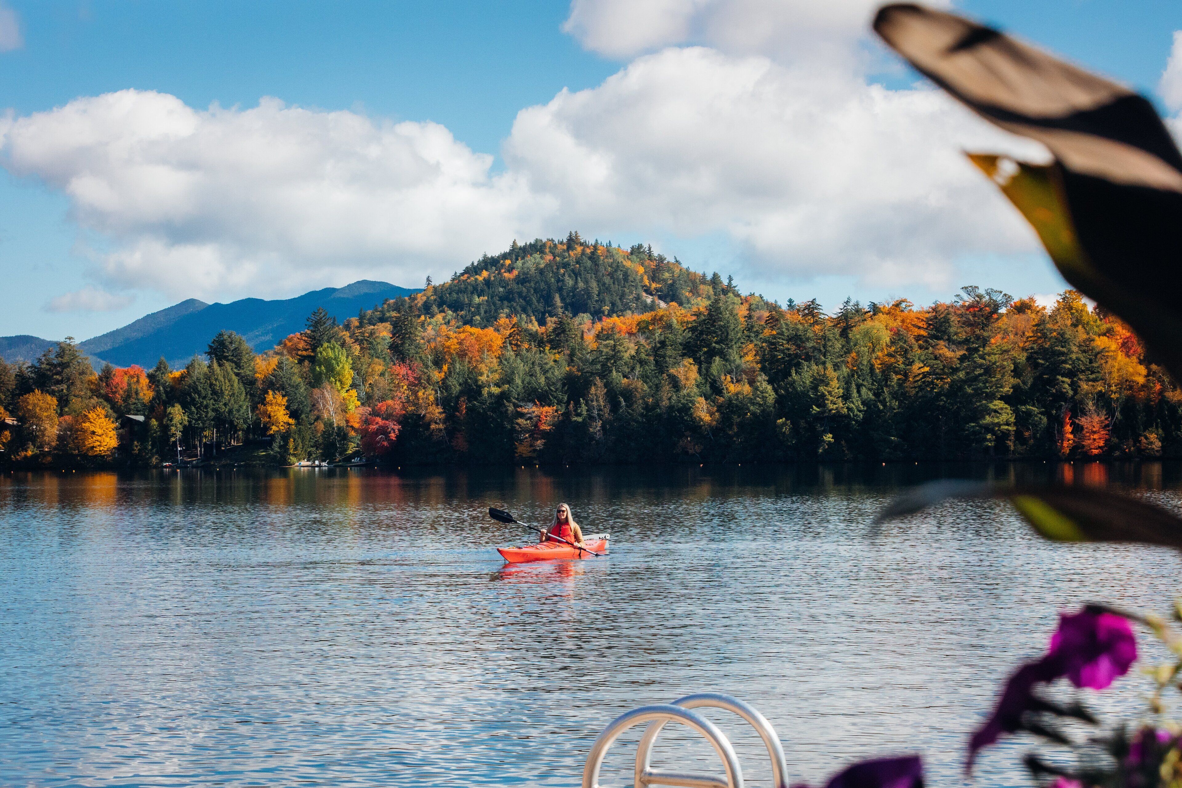 A kayaker on a calm lake with autumn foliage and mountains in the background.
