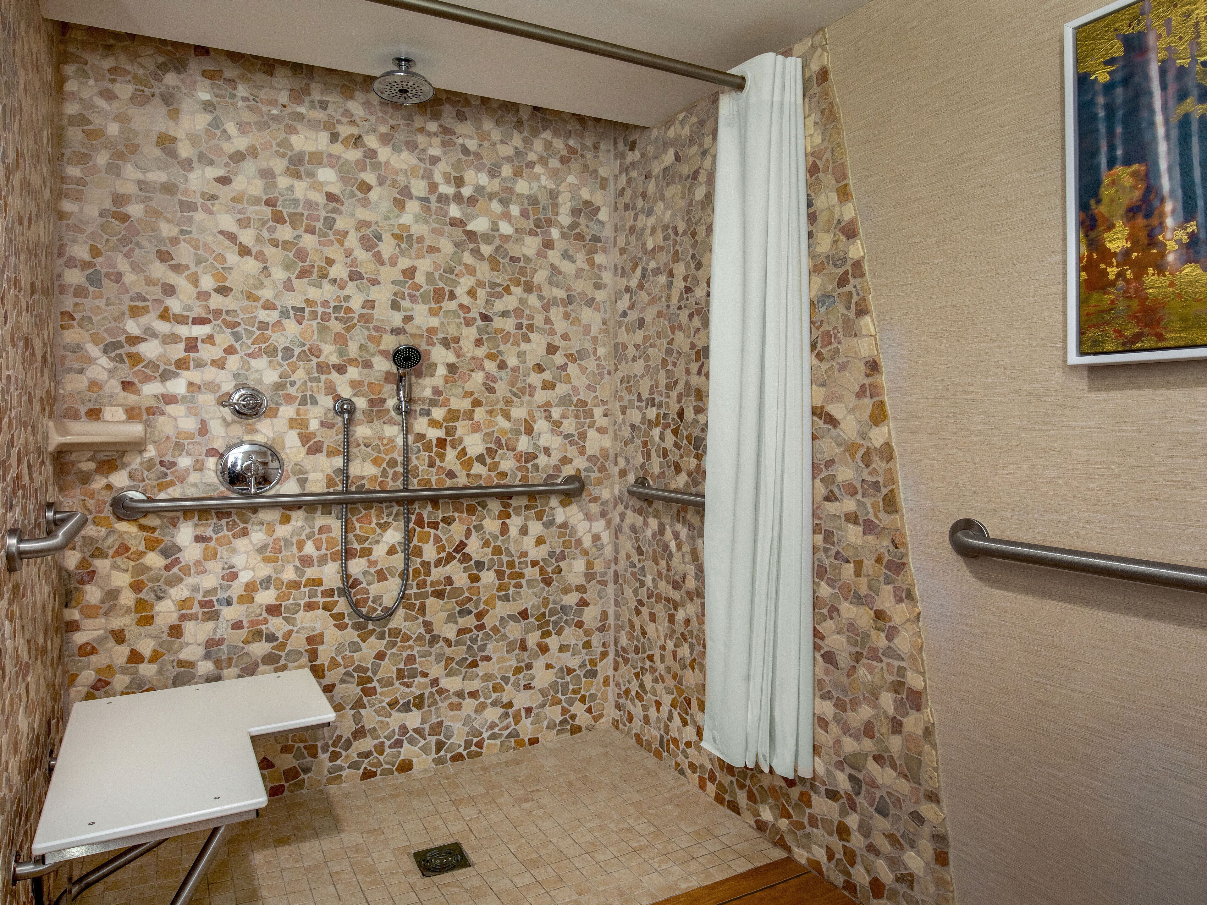 A shower area with mosaic tile walls, a white shower curtain, and a grab bar.
