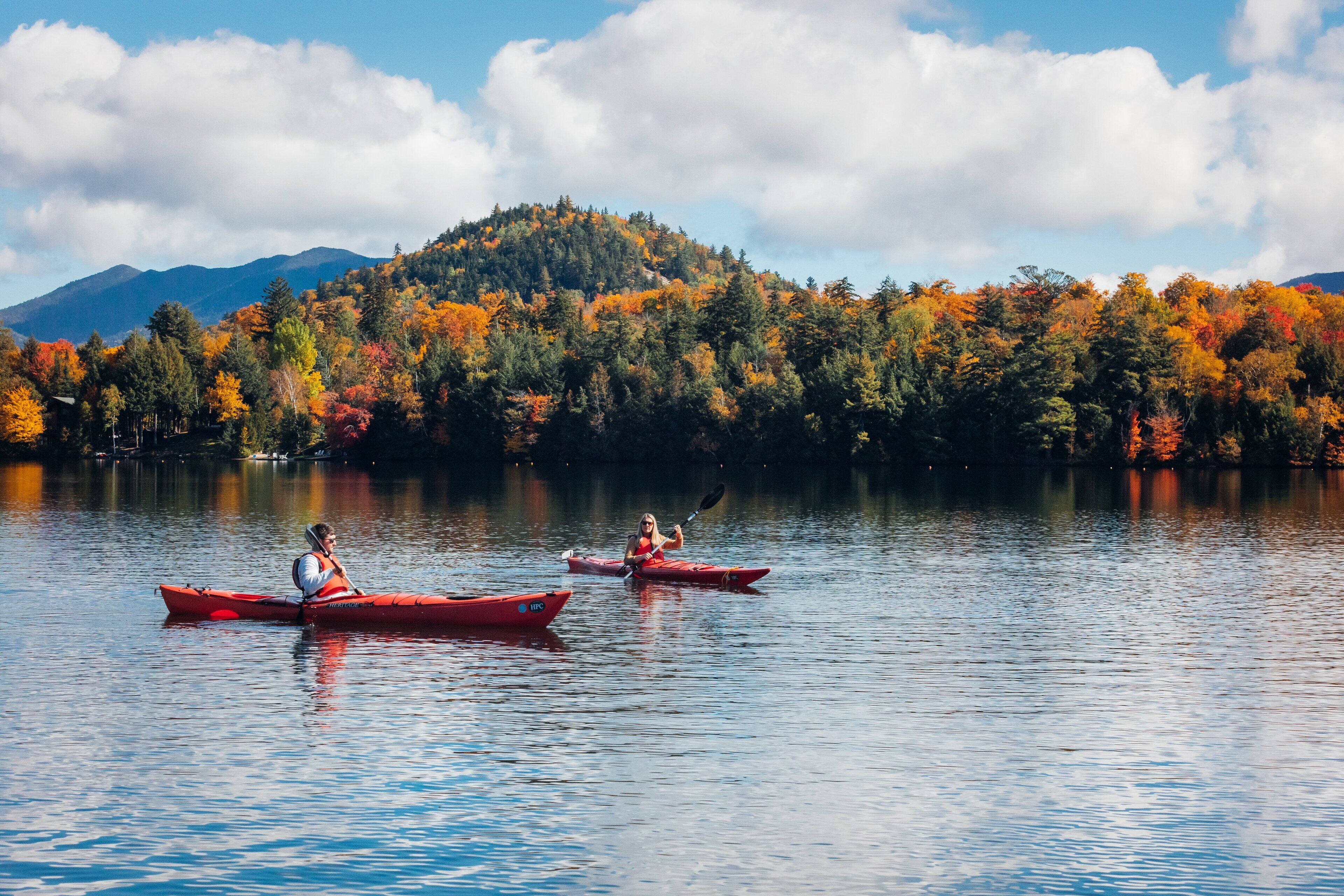 Two kayaks on a calm lake with a forested mountain in the background.