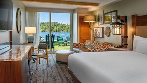 A hotel room with a large bed, a desk with a TV, a sofa, and a view of a lake. - High Peaks Resort (Lake Placid)