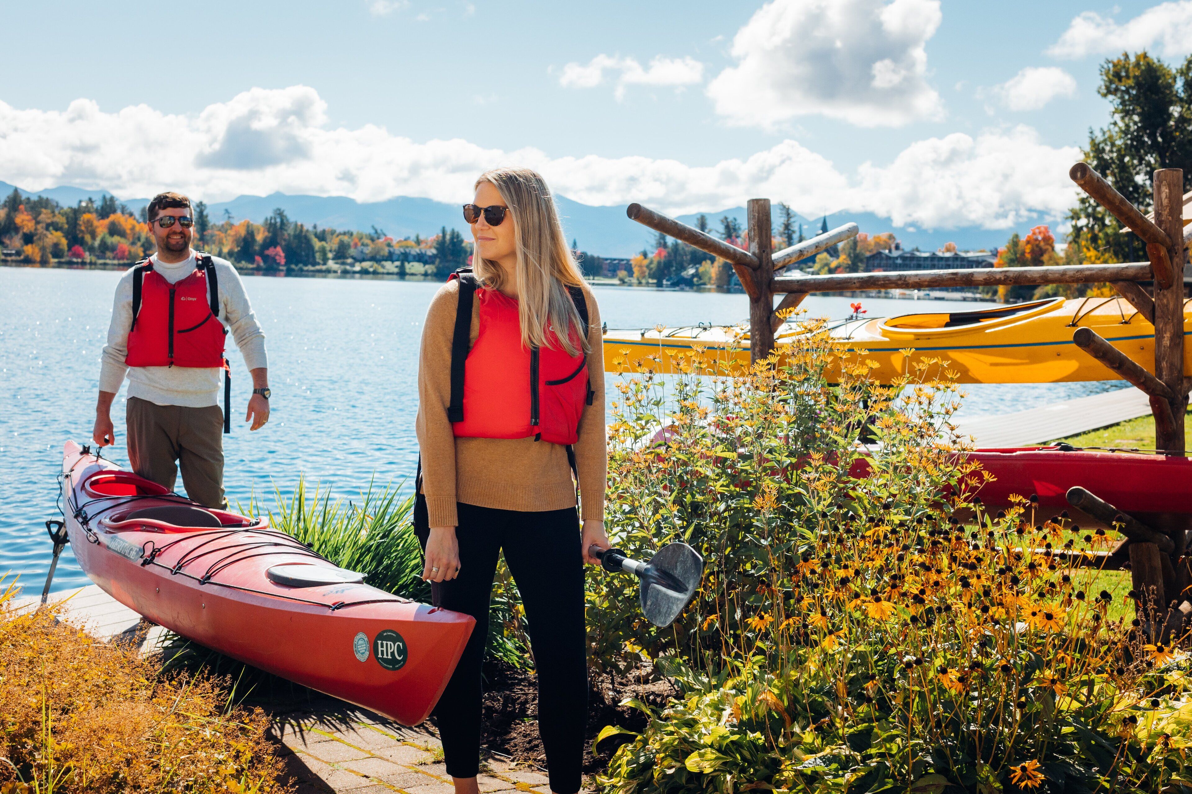 A lakeside scene with a red kayak, a yellow kayak, and a wooden dock.