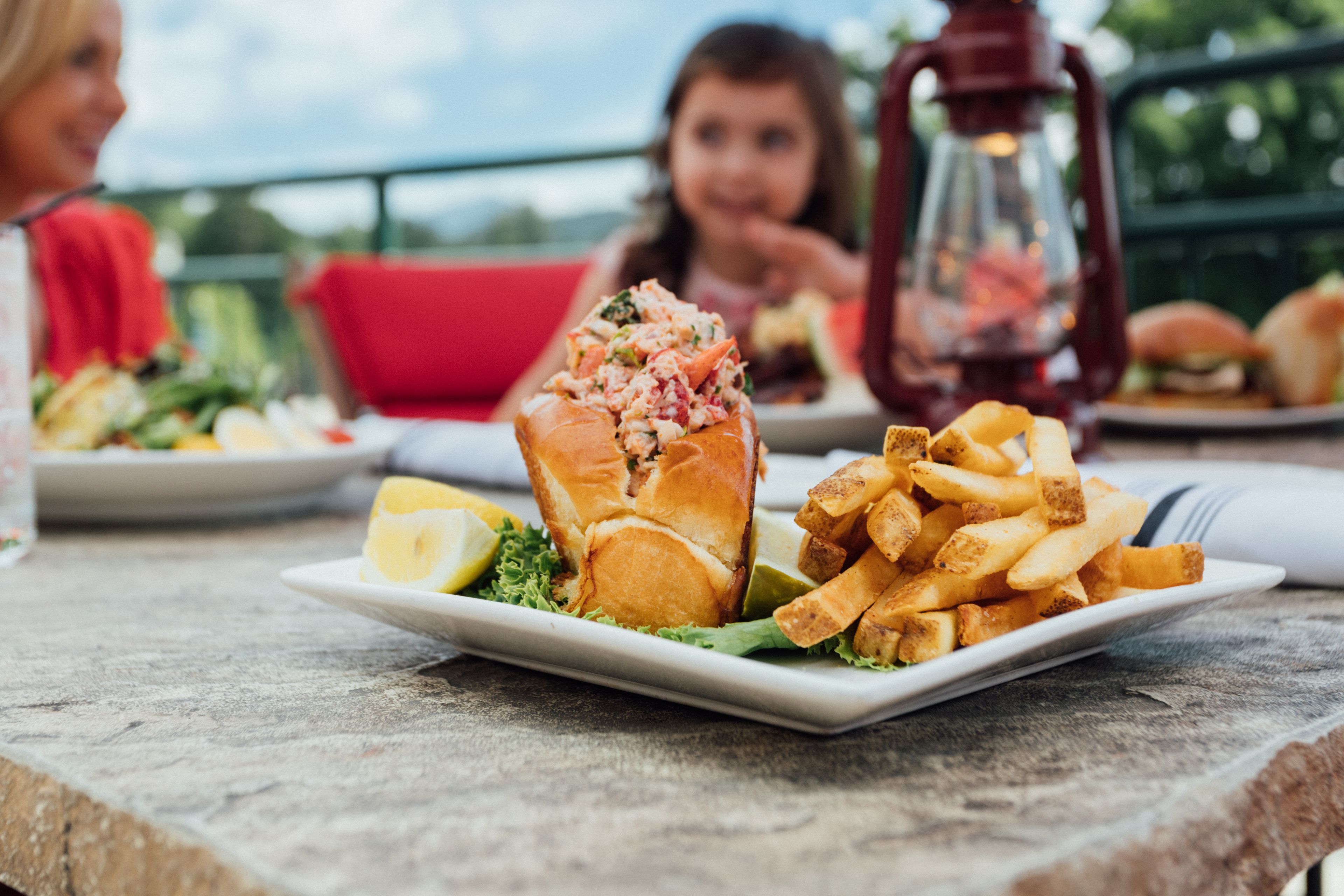 Une table à manger avec une assiette de nourriture, comprenant un sandwich au homard et des frites, et une chaise rouge en arrière-plan.