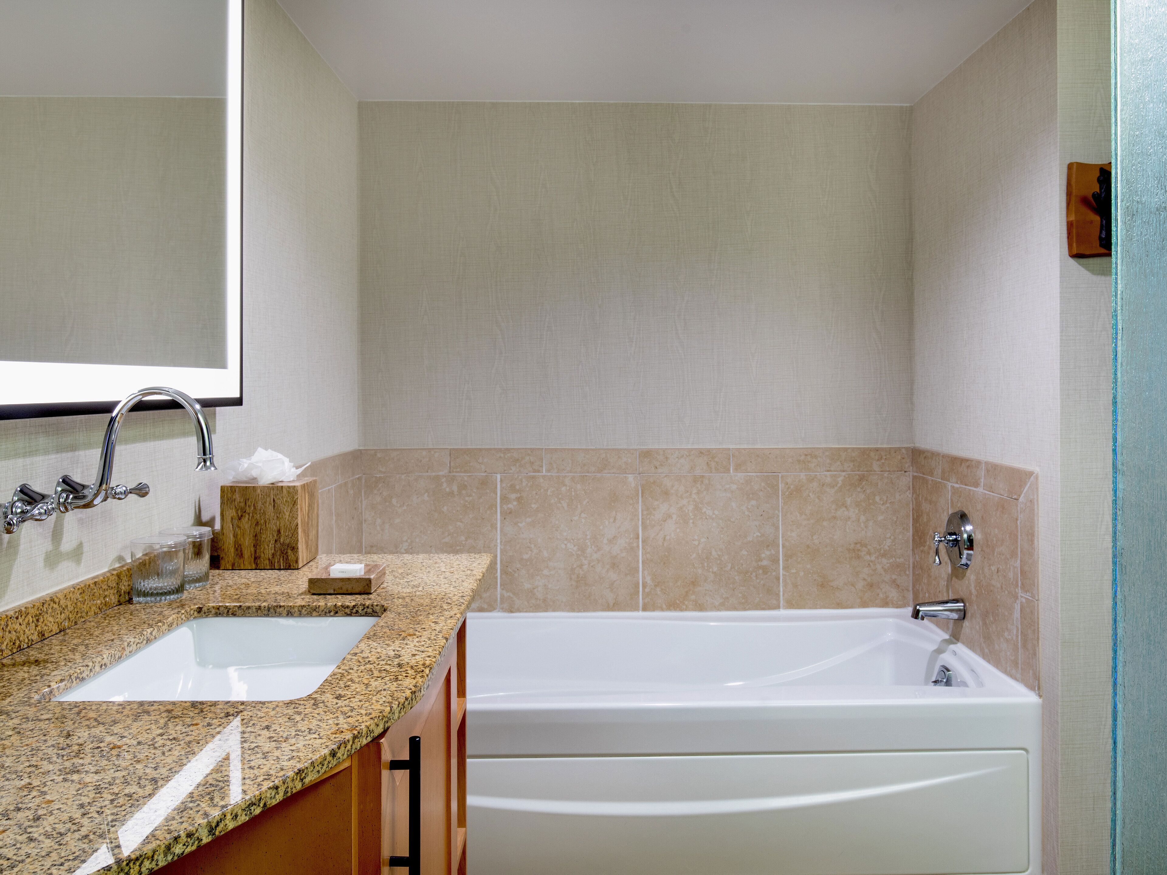 A bathroom with a granite countertop, two sinks, a mirror, and a bathtub.