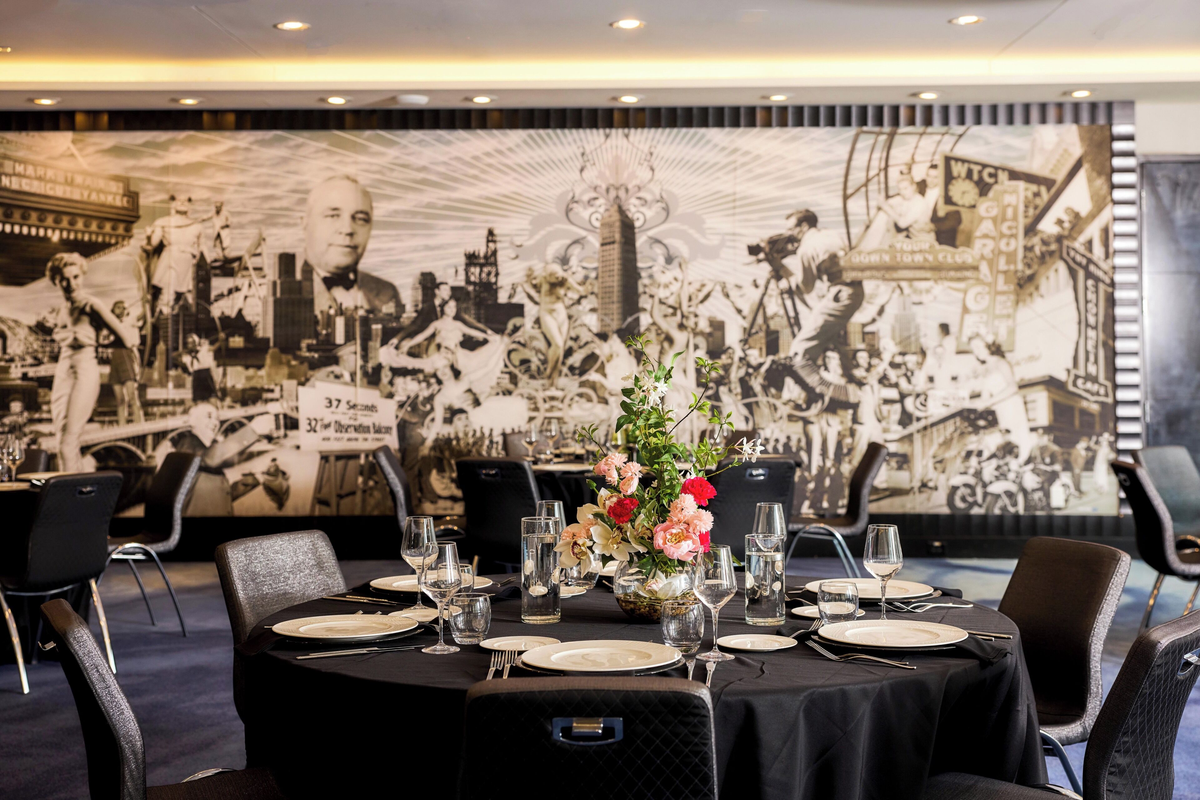 A dining area with round tables set for a meal, featuring a large mural on the wall behind.