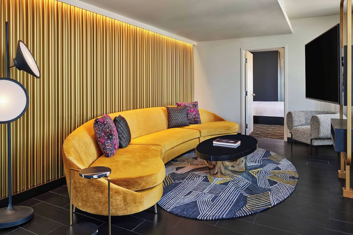 Uma sala de estar moderna com um sofá amarelo curvo, uma mesa de centro redonda e um tapete estampado.