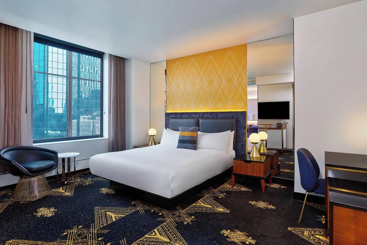 Quarto de hotel com uma cama grande, uma escrivaninha, uma cadeira e uma televisão.