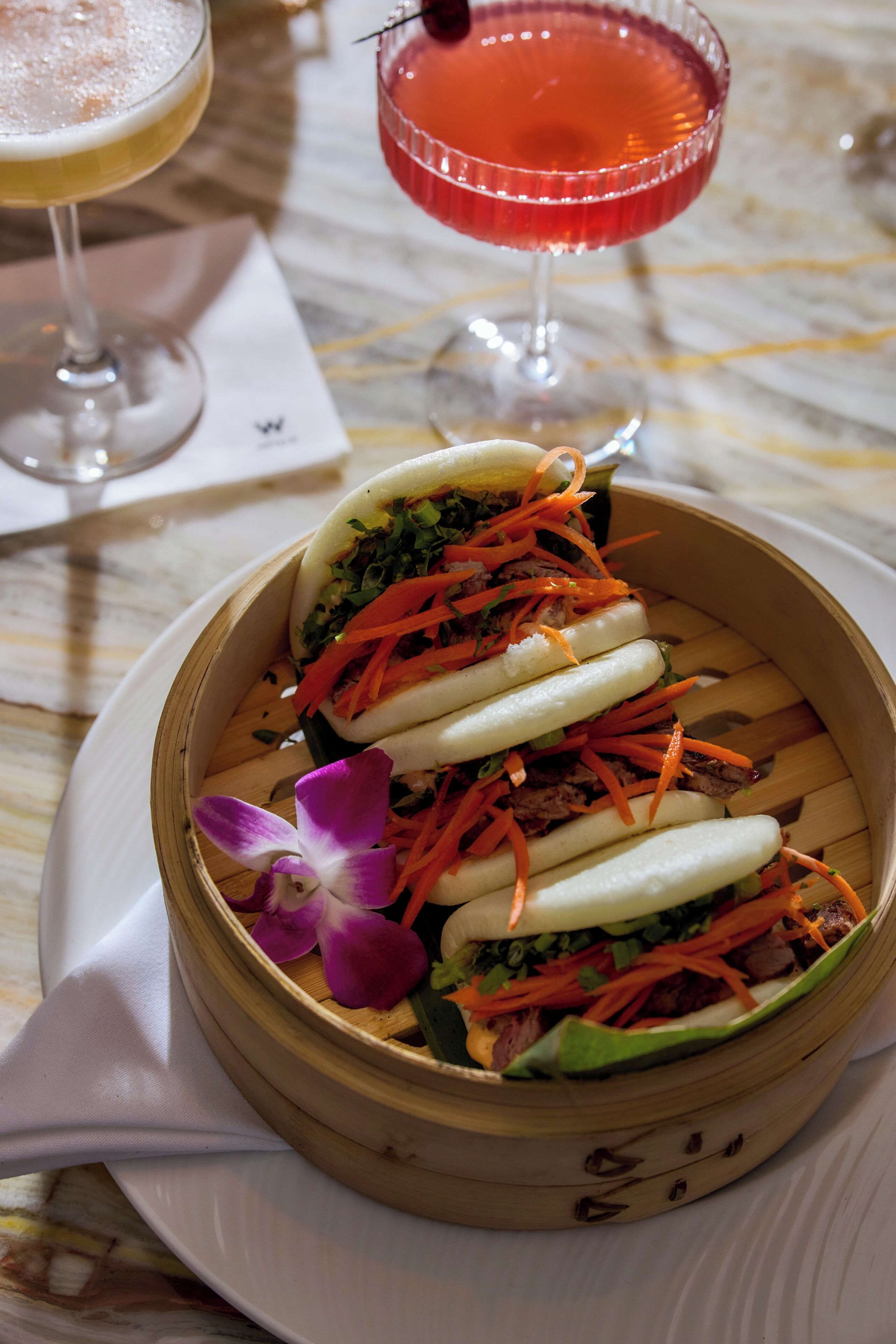 A bamboo steamer with food, a cocktail glass, and a menu on a table.