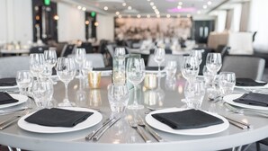 Ein Restaurant mit runden Tischen, gedeckten mit weißen Tellern, schwarzen Servietten und klaren Gläsern.