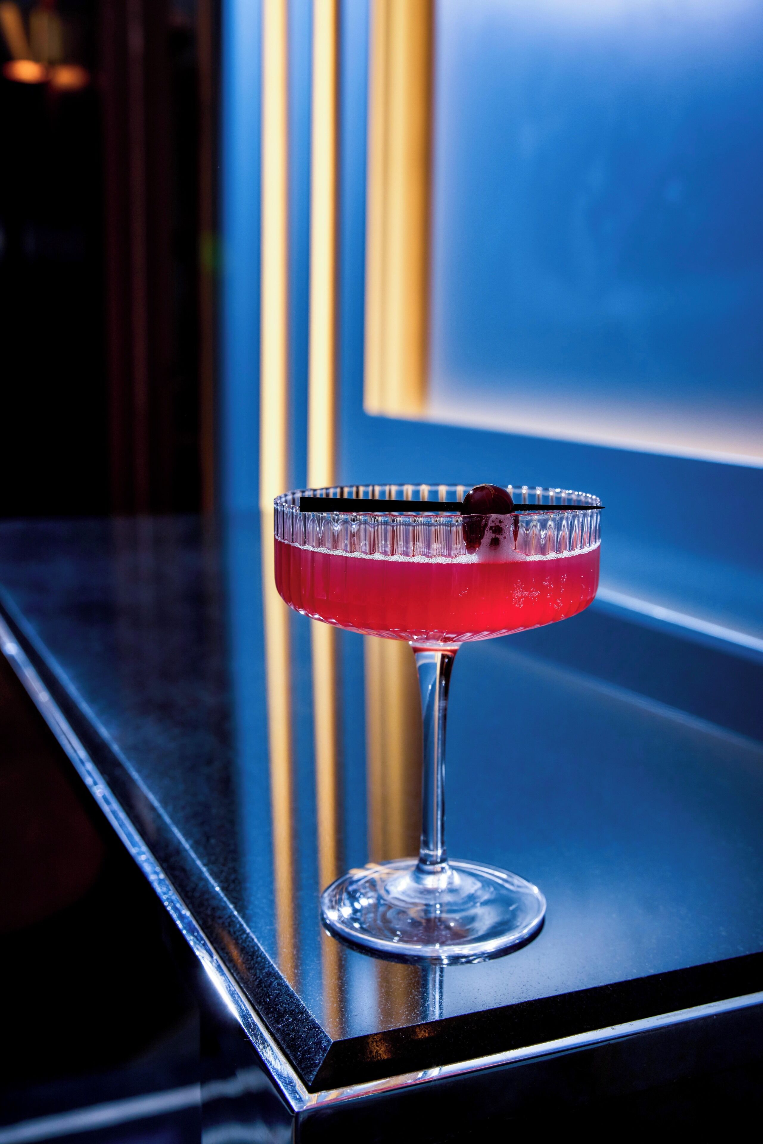 Un vaso de cóctel con una bebida roja sobre una superficie reflectante.