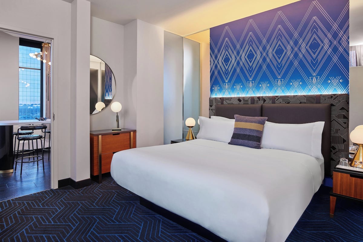 Quarto de hotel com uma cama grande, uma escrivaninha com cadeira, um espelho e um papel de parede estampado.