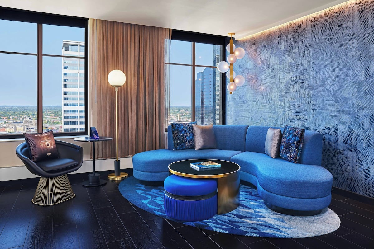 Uma sala de estar moderna com um sofá azul, uma mesa de centro redonda e vista para a cidade através de grandes janelas.