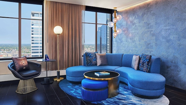 Ein modernes Wohnzimmer mit einem blauen Sofa, einem runden Couchtisch und Blick auf die Stadt durch große Fenster.