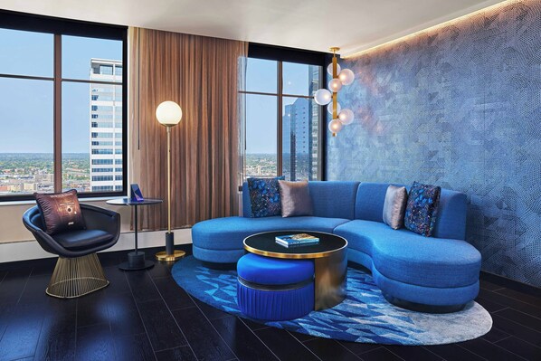 Un salon moderne avec un canapé bleu, une table basse ronde et une vue sur la ville grâce à de grandes fenêtres.